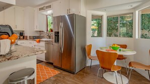 A modern kitchen with stainless steel appliances, white cabinetry, and a dining area with orange chairs. - ATOMIC-MOD HOUSE in prime Palm Desert/next to El Paseo! (Palm Desert)