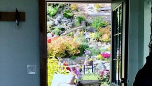 An open door leading to a patio with a wooden deck, a chair, and a view of a landscaped garden with rocks and plants.