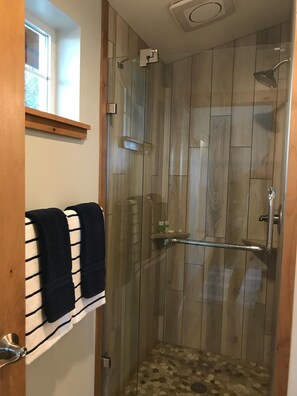 Una ducha con cerramiento de vidrio, suelo de madera y un pequeño estante con artículos de tocador.
