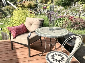 Una terraza de madera con una silla acolchada y una mesita con un jarrón de flores.