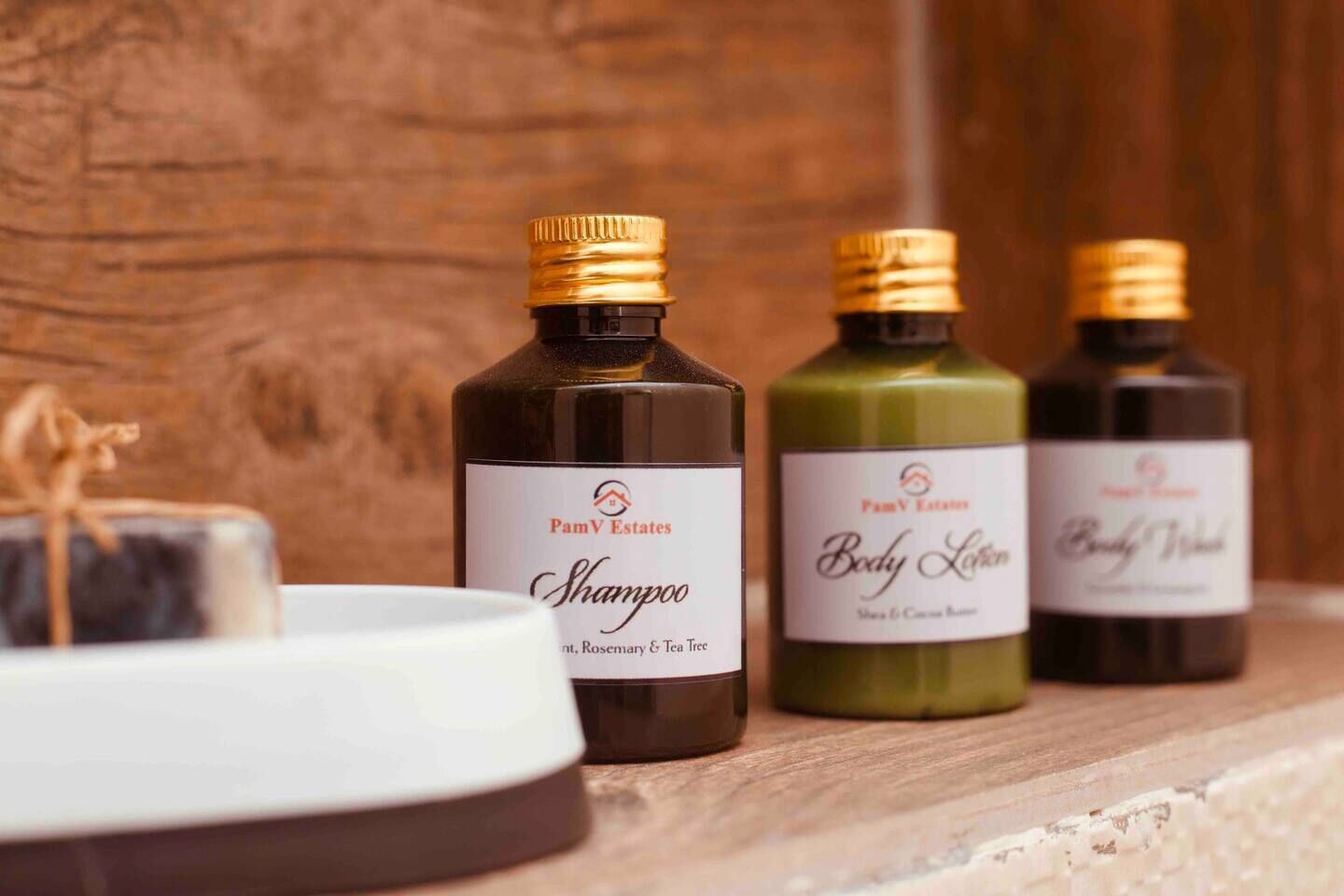 Three bottles of PamV Estates body care products on a wooden shelf.