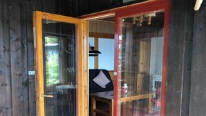 Une cabane en bois avec une porte vitrée donnant sur un coin repas équipé d’une table et de chaises.
