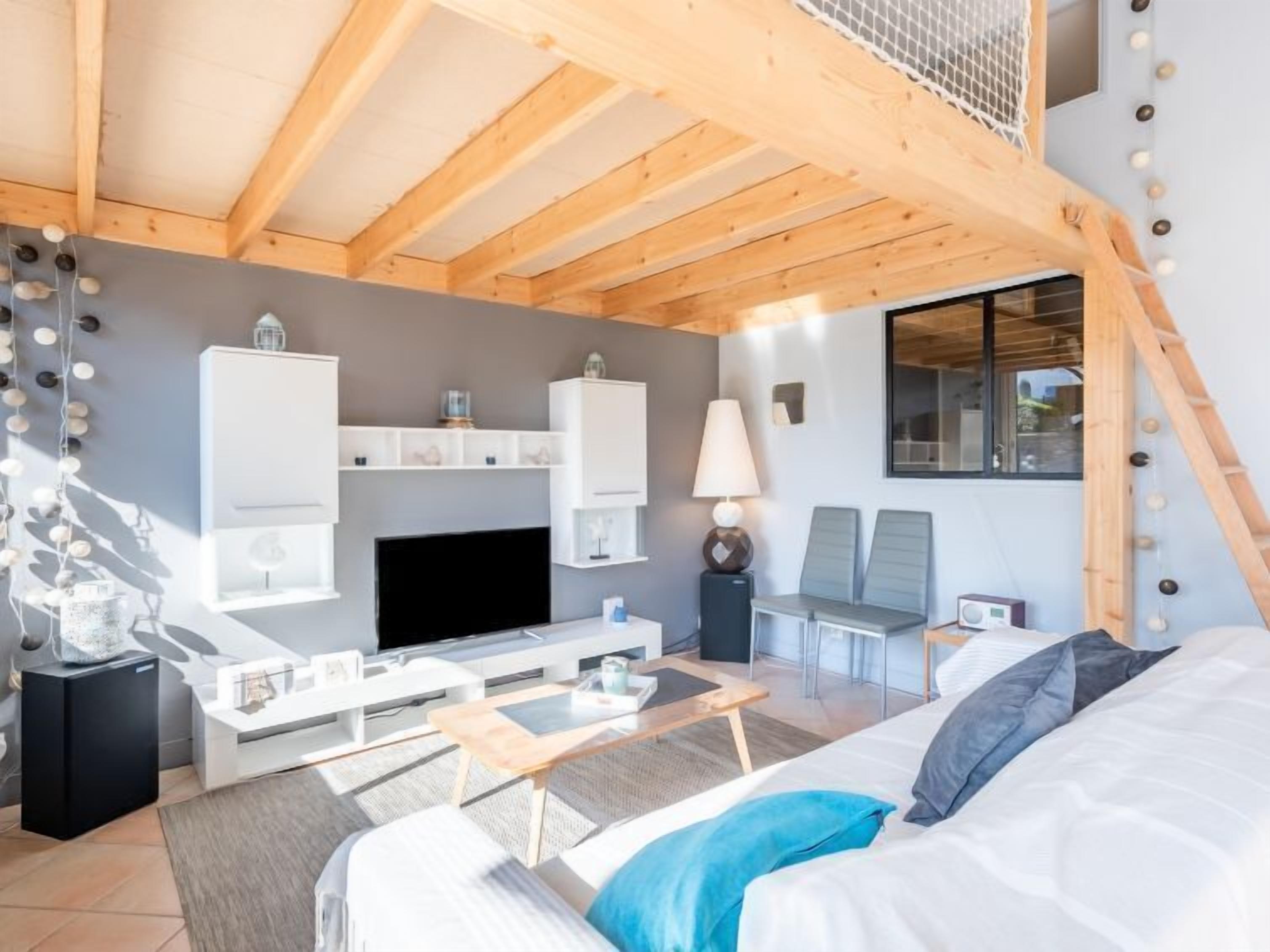 A modern hotel room with a wooden ceiling, a flat-screen TV, a bed, a desk, and a chair.