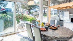 Un coin repas avec une table dressée pour quatre personnes, entourée de chaises, et une vue sur l’extérieur grâce à de grandes portes-fenêtres coulissantes.