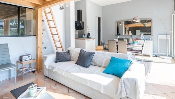 Un salon moderne avec un plafond en bois, un canapé avec des coussins, une petite table avec une radio et, au fond, un coin cuisine.
