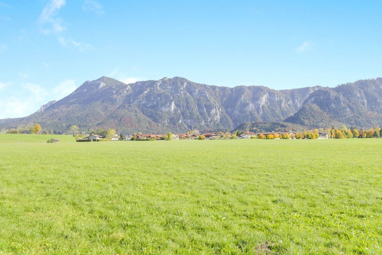 A rural landscape with a mountain range in the background, a green field in the foreground, and a row of houses with red roofs.