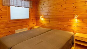 Ein Schlafzimmer einer Holzhütte mit einem Bett, einem Fenster mit Jalousien und zwei Wandleuchten.