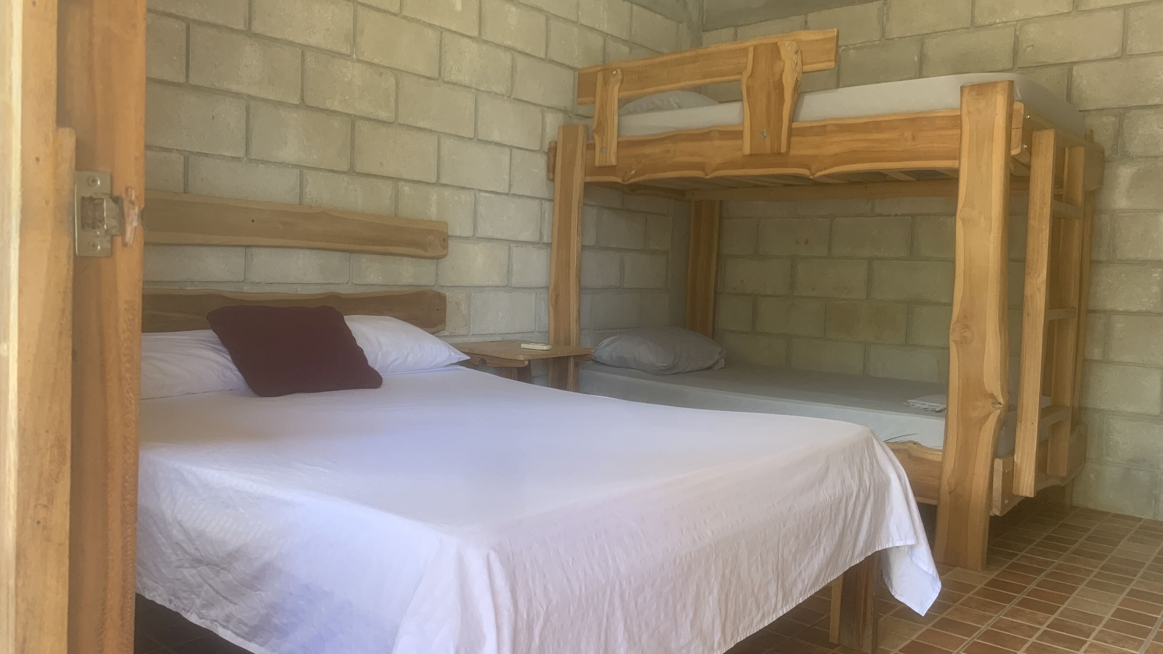 A room with a bunk bed, a single bed, and a nightstand with a remote control.