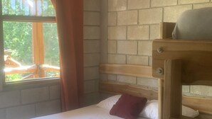 Een enkel bed met een houten hoofdbord, een raam met gordijnen, en een bakstenen muur.
