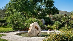 A garden with a central rock feature, a pond, and various plants.