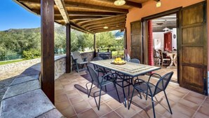 An outdoor patio with a wooden pergola, a table with chairs, and a view of the surrounding landscape.