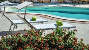 A poolside area with lounge chairs and towels, surrounded by a stone wall and greenery.