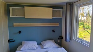 Un dormitorio con dos camas, una ventana con vistas a la vegetación y un estante sobre las camas.