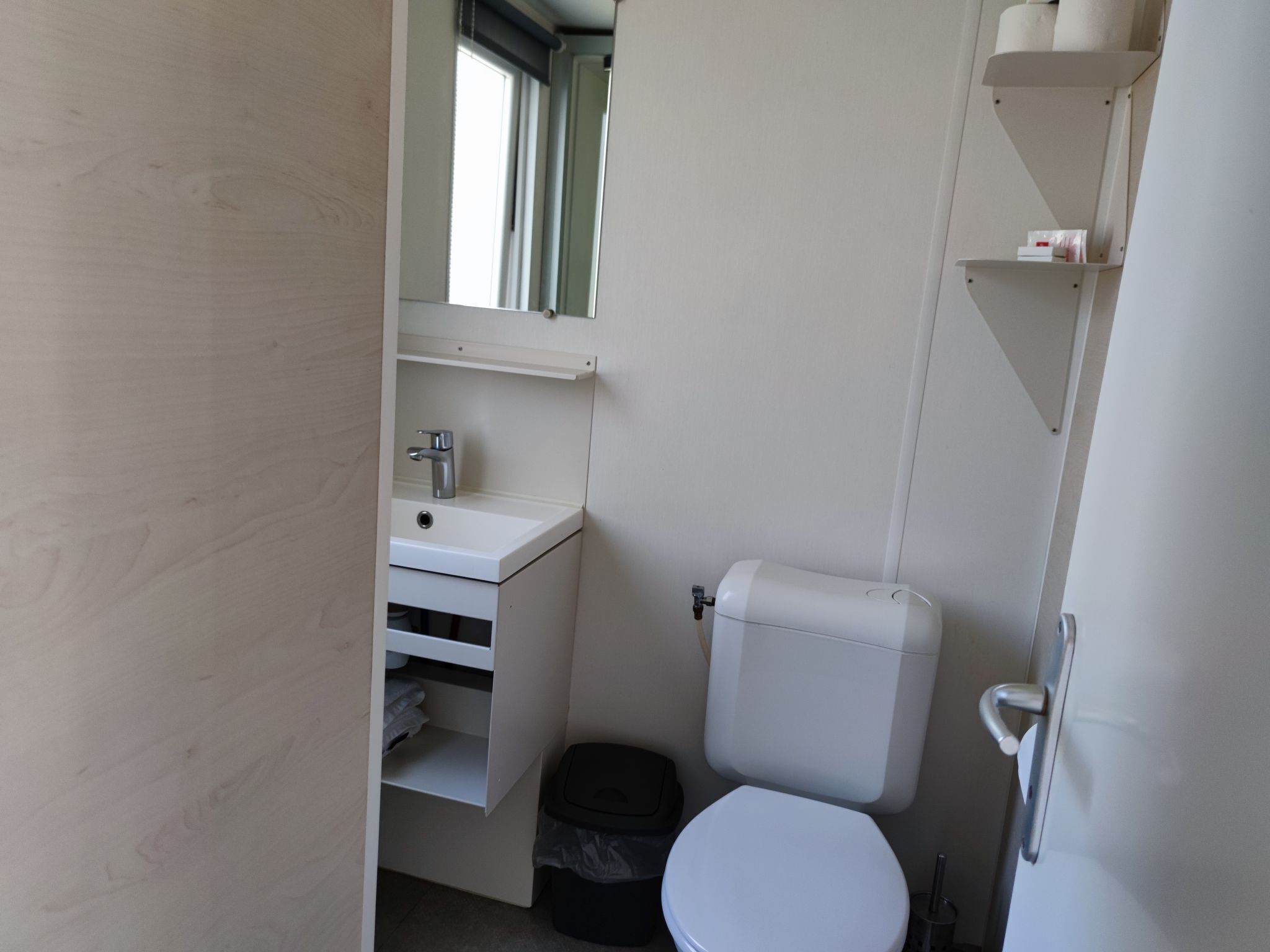 A compact bathroom with a toilet, sink, and storage shelves.