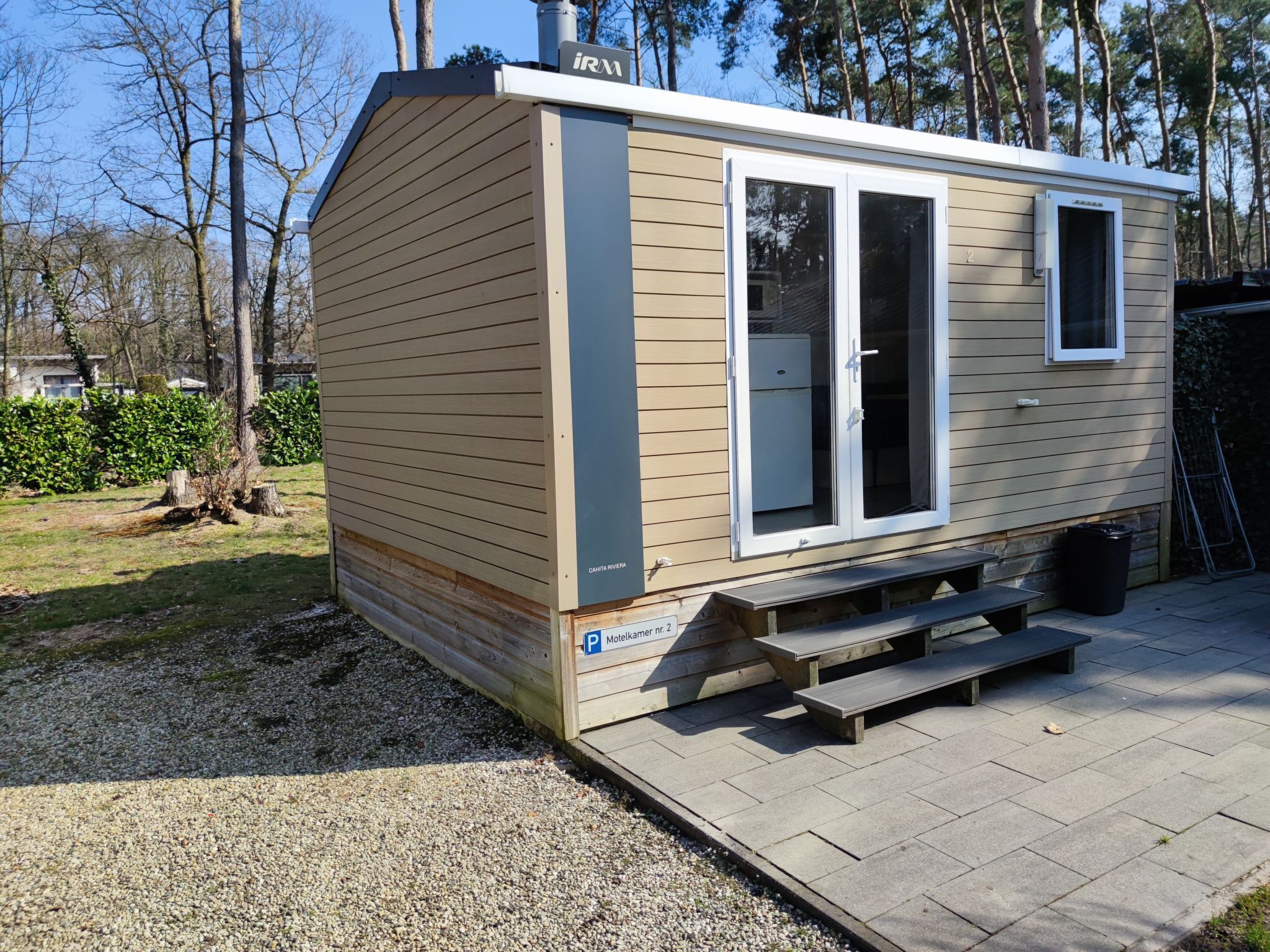 Un petit motel d’un seul étage, avec une façade en bois, une terrasse couverte et une allée gravillonnée.