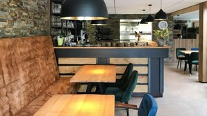 Un café moderno con mesas de madera y asientos acolchados, una zona de bar con equipamiento de cocina y un ambiente relajado.