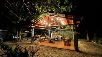 A covered outdoor seating area with tables and chairs, a hammock, and a small bar area with stools.
