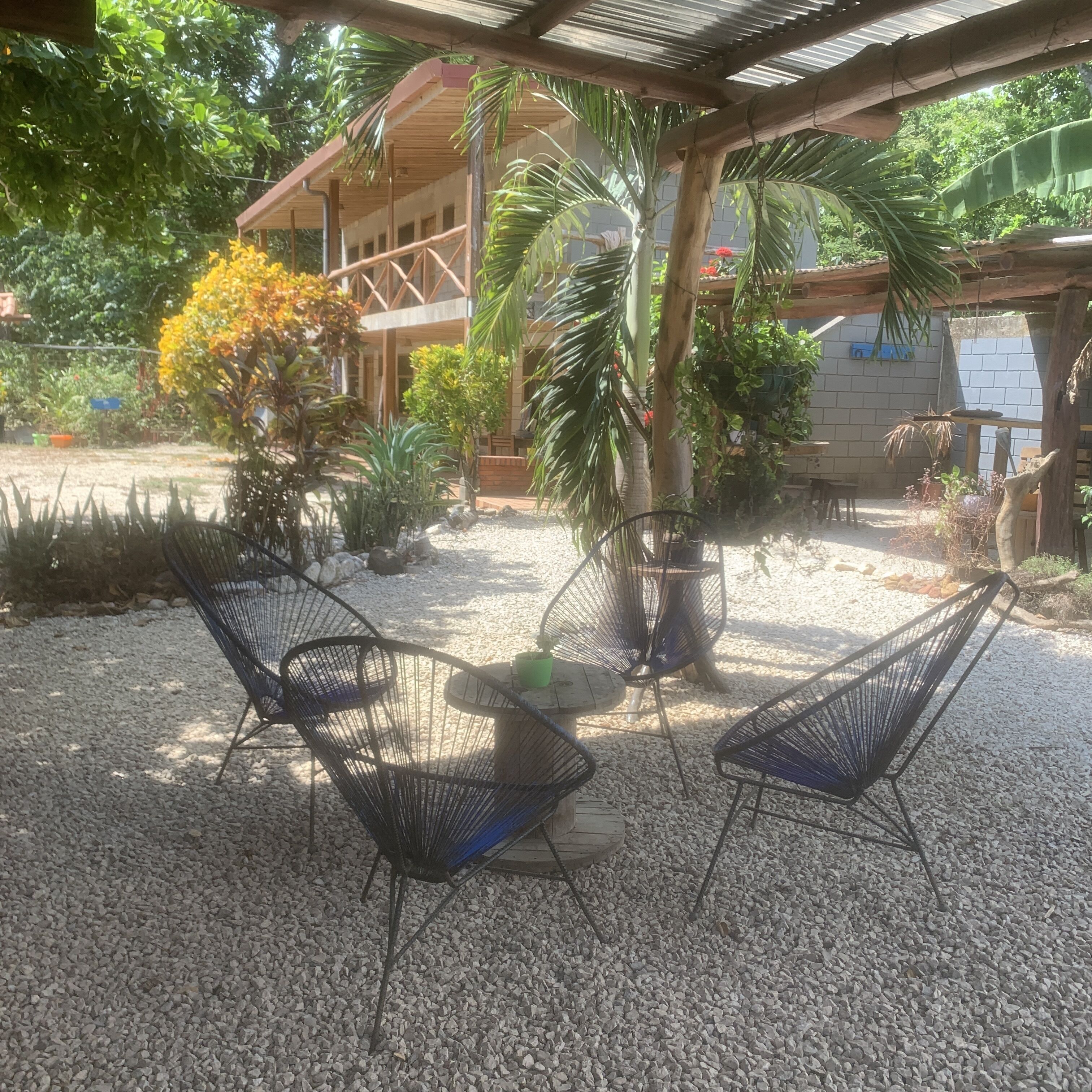 Een terras met metalen stoelen en een ronde tafel, omringd door grind en verschillende planten.