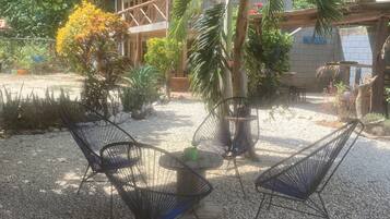 Een terras met metalen stoelen en een ronde tafel, omringd door grind en verschillende planten.