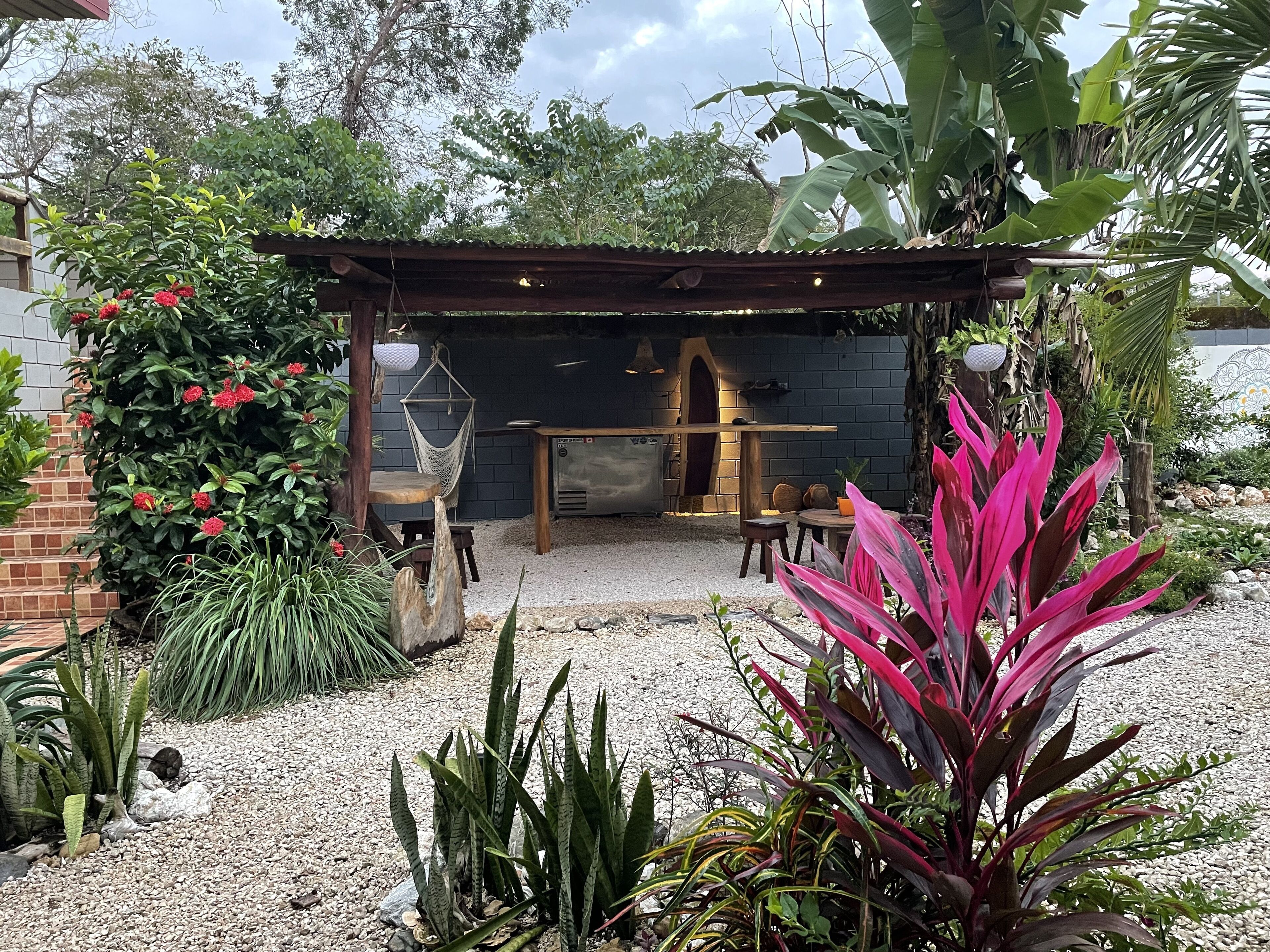 A patio area with a stone oven, wooden furniture, and a hanging chair.