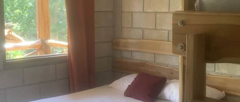 A single bed with a wooden headboard, a window with curtains, and a brick wall.