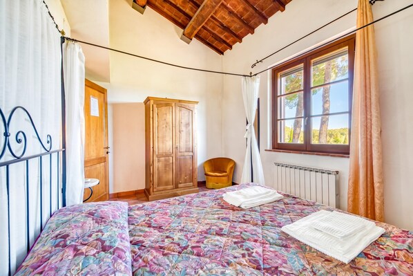 A bedroom with a bed, wooden wardrobe, window with curtains, and a radiator. - Apartment Alloro Shared Pool for 4 pax, Castiglione del Lago, Italy (Castiglione del Lago)