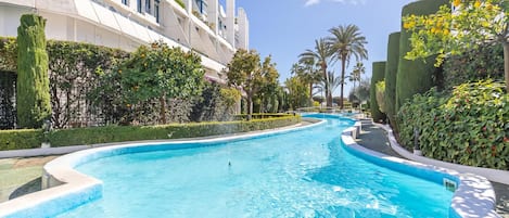 Une piscine à bord incurvé, entourée d’arbustes bien entretenus et de palmiers.