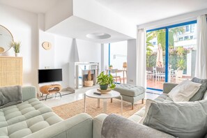 Ein modernes Wohnzimmer mit einer Couch, einem Couchtisch, einem Fernseher und Blick auf die Terrass.
