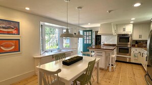 Een moderne keuken met witte kasten, een houten aanrecht en roestvrijstalen apparatuur. Er is een eethoek met een witte tafel en stoelen.
