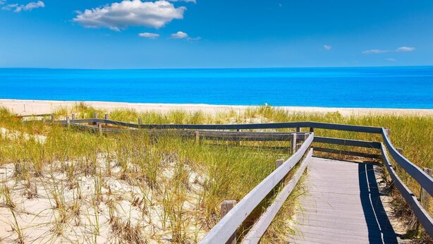 Een houten looppad naar een strand met helderblauw water en een zandstrand.