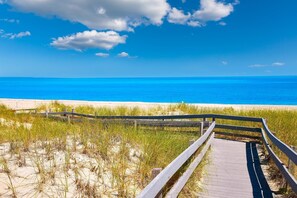 A wooden boardwalk leading to a beach with clear blue water and a sandy shore.