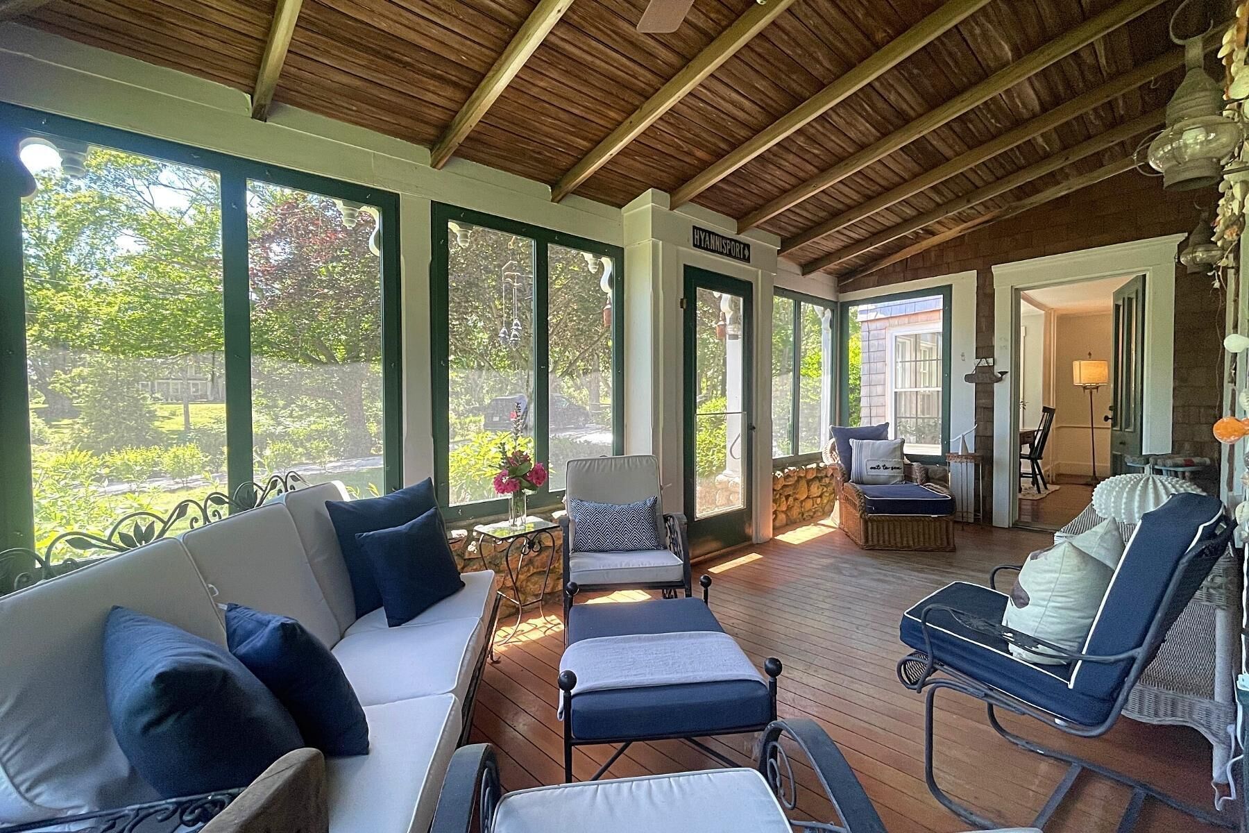 A covered outdoor seating area with a wooden ceiling, large windows, and a view of greenery.