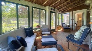 Een overdekt terras met houten plafond, grote ramen en uitzicht op groen.