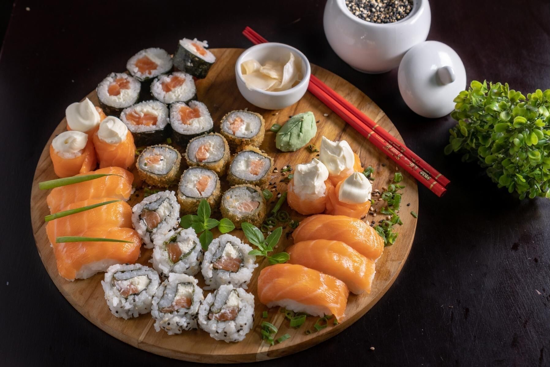 Ein Holzbrett mit verschiedenen Sushi-Stücken, darunter Lachs und Rollen, garniert mit grünen Kräutern und Sesam.