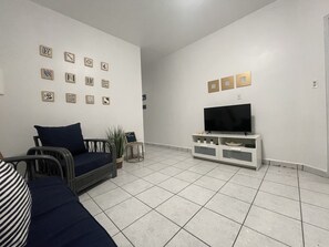 A living room with a sofa, a TV on a white stand, and a wall decorated with various framed items. - Located on the SouthWest Side of Puerto Rico (cabo rojo)