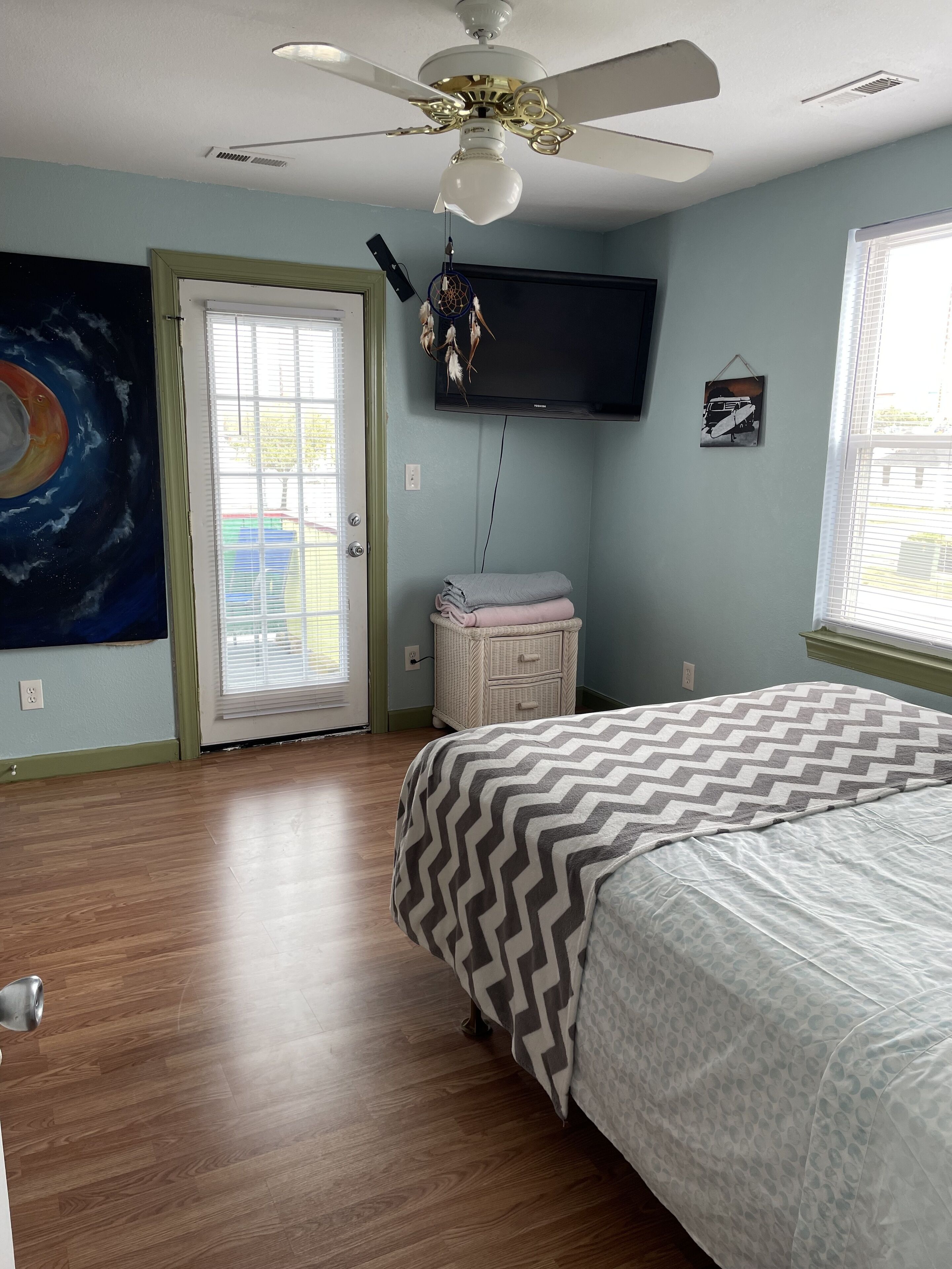 A bedroom with a bed, a ceiling fan, a television, and a door leading to a balcony.