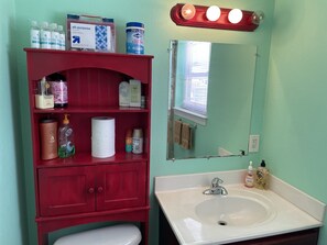 A bathroom with a red cabinet containing toiletries, a white sink, and a mirror with lights above it.