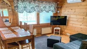 Ein gemütliches Blockhaus-Interieur mit einem Holzespeise-Tisch, Stühlen, einer Couch, einem Fernseher und einem Fenster mit Jalousien.