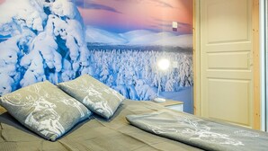 Huone, jossa on sänky, tyynyjä ja seinämaalaus, joka esittää lumista maisemaa.