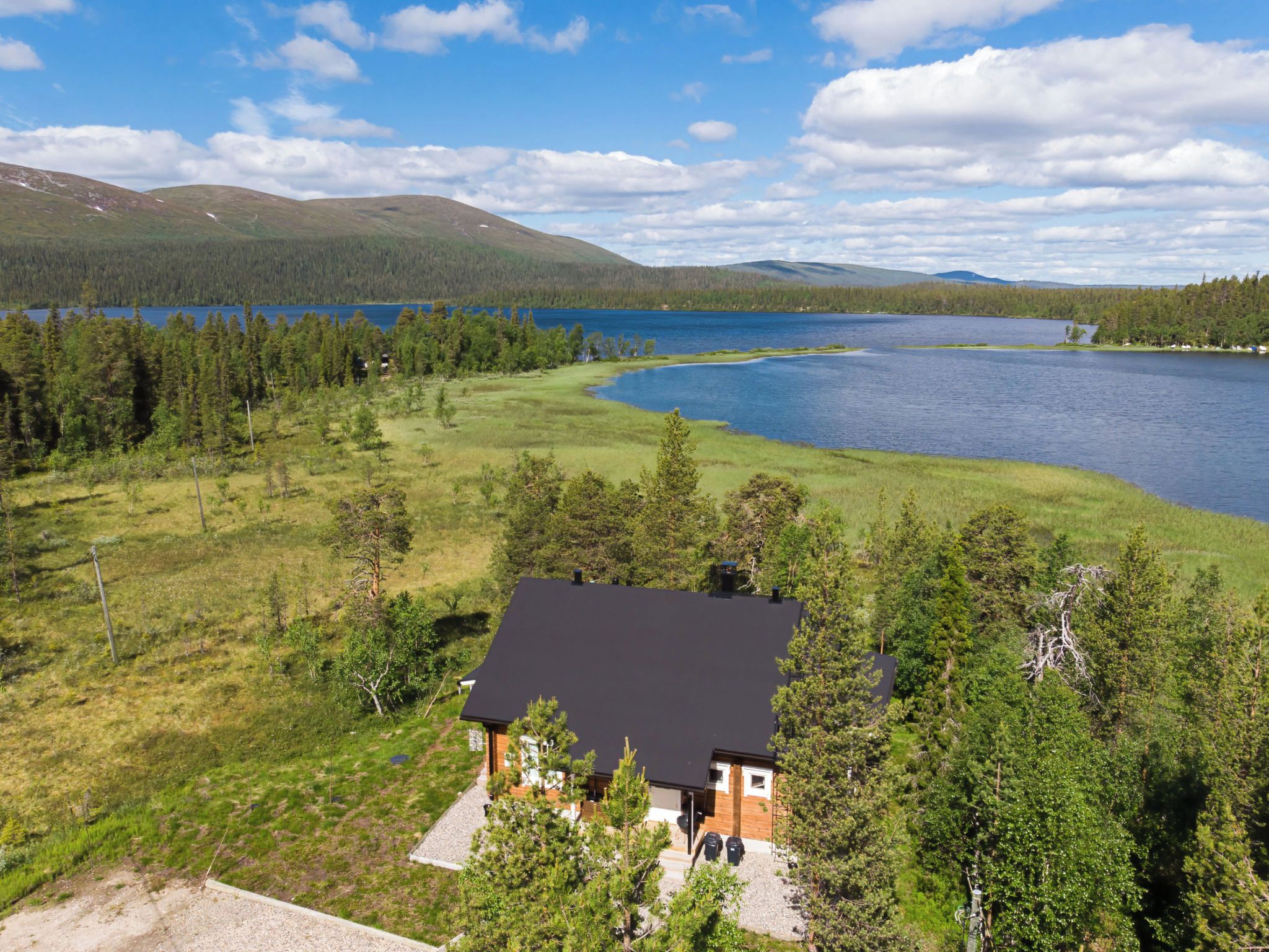 Una casa con techo negro, rodeada por un bosque y un lago.