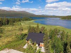 Una casa con techo negro, rodeada por un bosque y un lago.