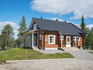 En stuga byggd av trä med ett stort glasfönster, en veranda och en grusuppfart.