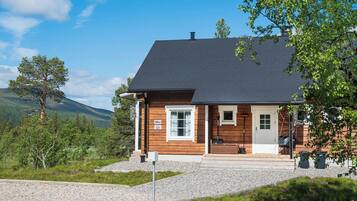 Puuinen mökki, jossa on kalteva katto, kuisti ja sorapäällysteinen ajotie.