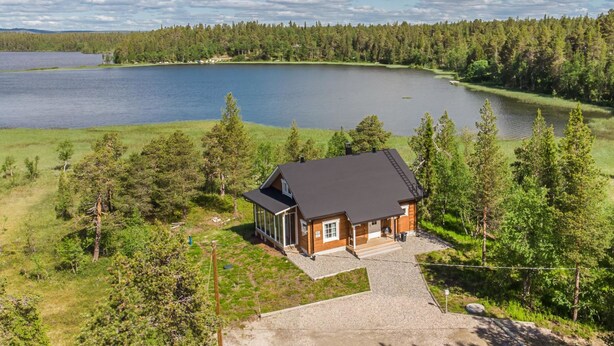 Mökki, jossa on suuri terassi, ja sen ympärillä on metsää ja järvi.