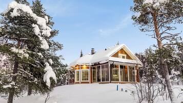 Lumipeitteinen mökki, jossa on puinen ulkoverhous, suuret ikkunat ja savupiippu.