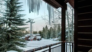 Une cabane en bois dotée d’un balcon donnant sur un paysage enneigé, avec un télésiège visible au loin.
