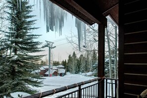 Une cabane en bois dotée d’un balcon donnant sur un paysage enneigé, avec un télésiège visible au loin.