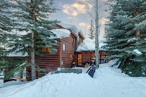 Une cabane en bois dotée d’un espace extérieur abrité, entourée d’arbres couverts de neige.