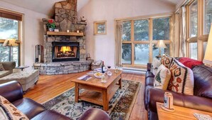Un salon chaleureux avec une cheminée en pierre, des meubles en cuir et de grandes fenêtres.