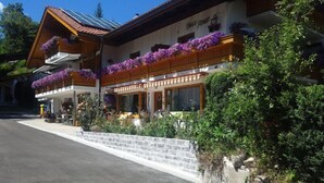 A traditional wooden building with a sloped roof, large windows, and flower boxes on the upper level.
